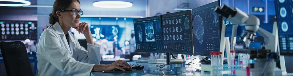 Woman in white lab coat looking at computer screens